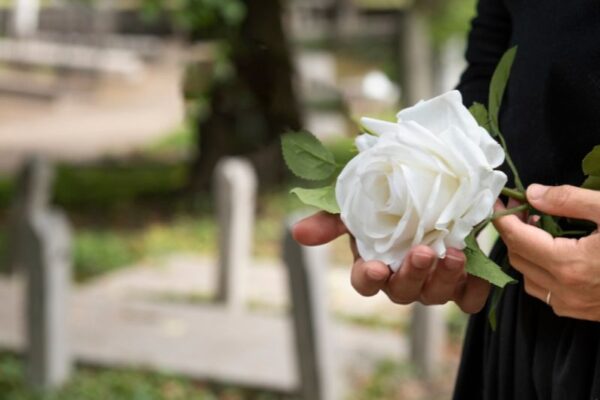 Picture of Mourning woman holding white flowers at her family grave in cemetery.