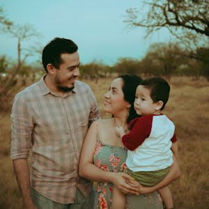 Family portrait of parents with child in warm outdoors setting, capturing joyful moments together.